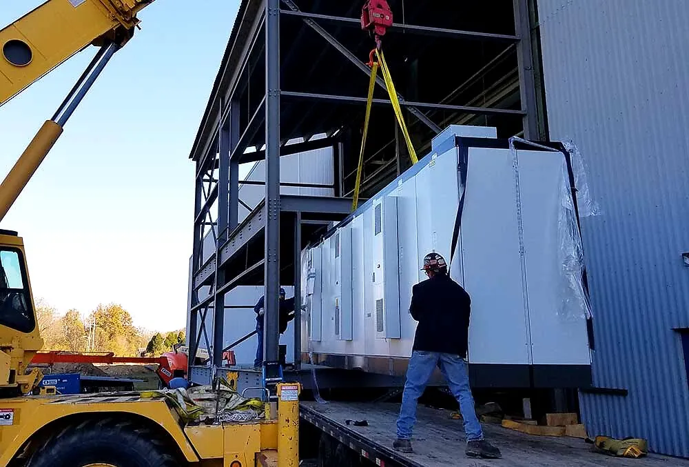 Crane setting a packaged electrical switchgear enclosure on a steel structure